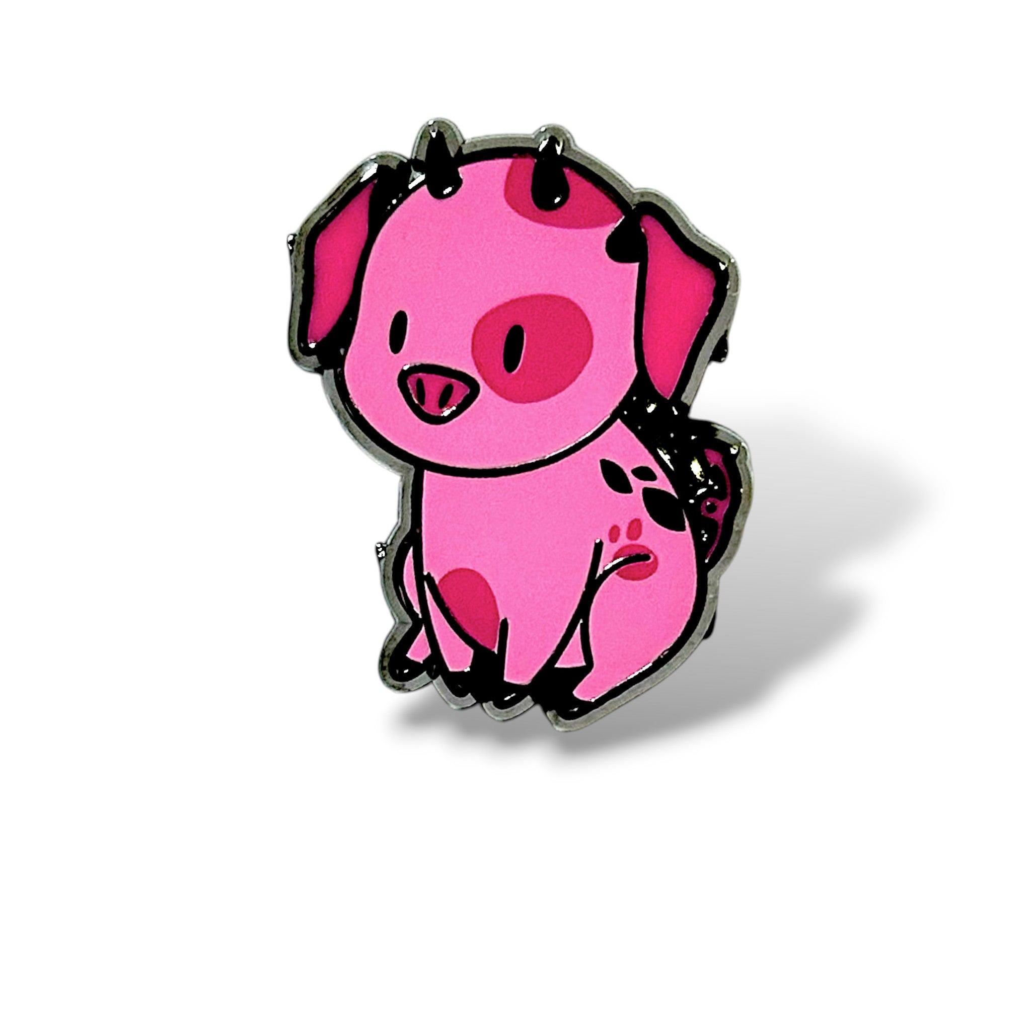 Cartoon-style enamel pin of a pink pig character named Fat Nuggets, designed in a cute and playful style. The pig has small black horns, large ears with black inner coloring, and several darker pink spots across its body. It is sitting upright with front legs straight, back legs bent, and a curly tail with black markings. The pig has a cheerful expression, outlined in black with a glossy enamel finish, capturing the whimsical “Angel-D pet” aesthetic.