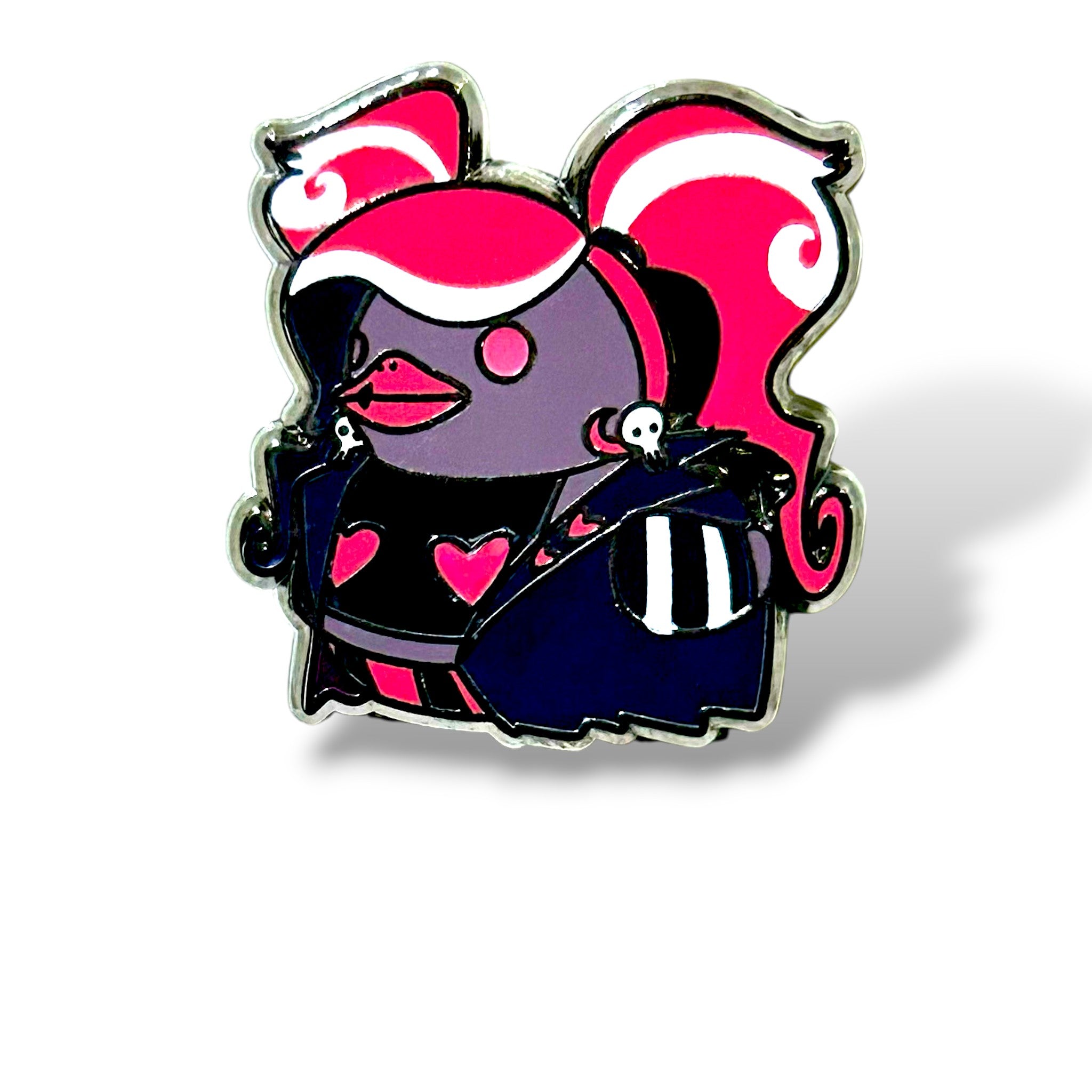 Cartoon-style enamel pin of a duck reimagined as a flamboyant fashionista character. The duck has a purple body with a bright pink-and-white voluminous hairstyle styled in curls. It wears a dark blue and black outfit decorated with heart shapes and skull motifs, including a cape with skull embellishments on the shoulders and striped sleeves. The design is bold, colorful, and gothic-punk inspired, making it a striking and playful collector’s piece.