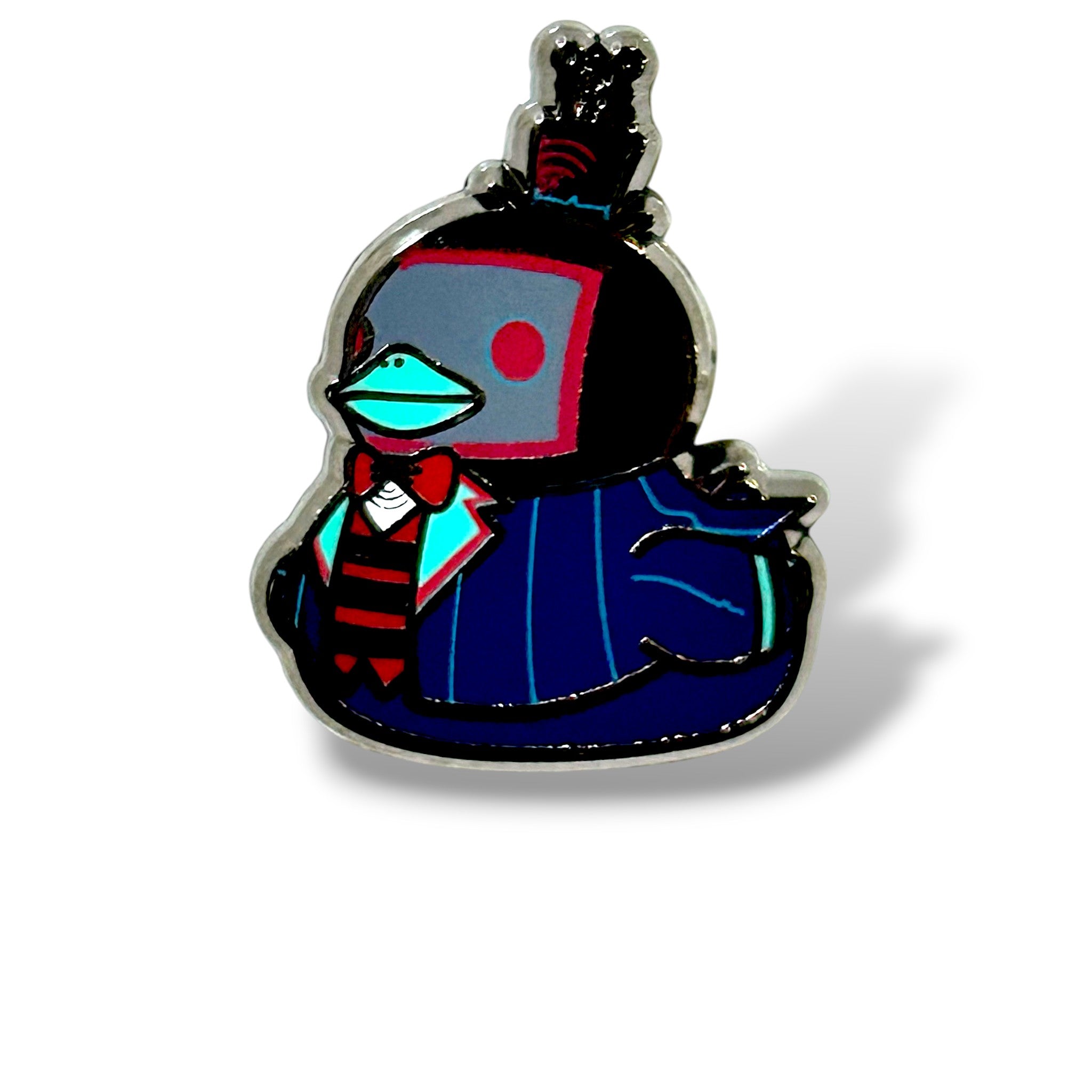 Cartoon-style enamel pin of a duck character dressed as a TV-themed demon. The duck has a black head with a red square on its cheek resembling a screen and wears a blue pinstripe suit with a red-and-black striped tie and turquoise bow tie. A tall top hat with a feather adds a formal touch, while the design is outlined in metal with a glossy enamel finish. The playful yet sinister look combines technology and fashion in a whimsical duck form.