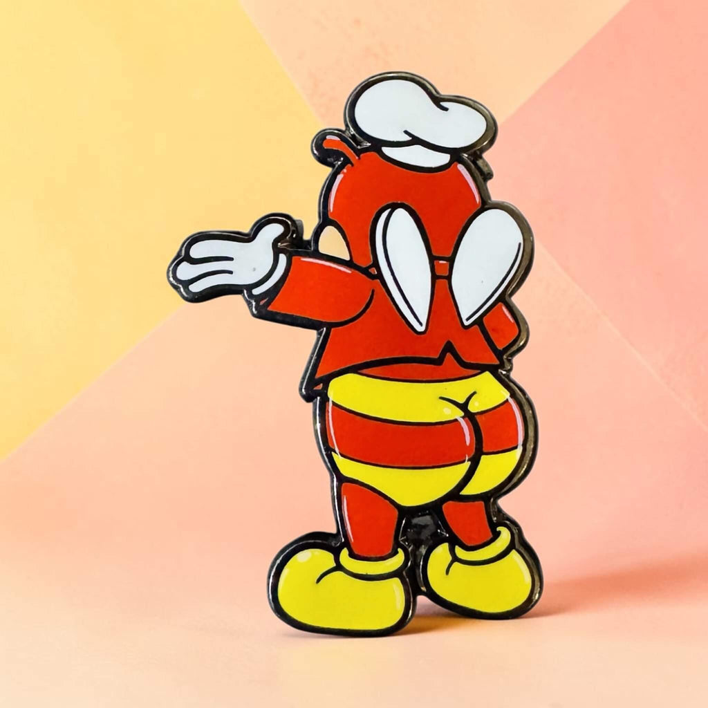 Jolli-Butt enamel pin showing a red character from behind in striped shorts, yellow shoes, and a white chef’s hat against a pastel yellow and peach background.