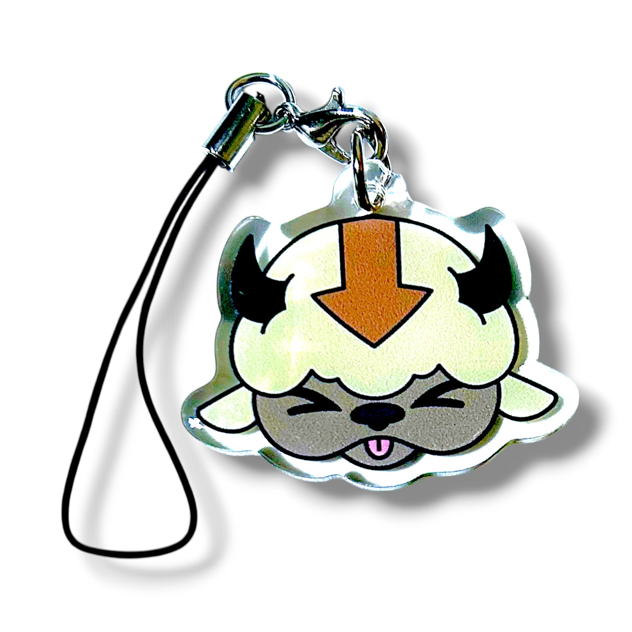 Cartoon-style keychain charm featuring a stylized fluffy creature with a white face, closed eyes, a protruding tongue, and a bold orange arrow on its forehead. The character has a rounded body and a soft, relaxed expression. It is attached to a black strap with a silver clasp. The design blends playful, air-themed aesthetics with cozy, animal-like features, making it a whimsical and collectible accessory.