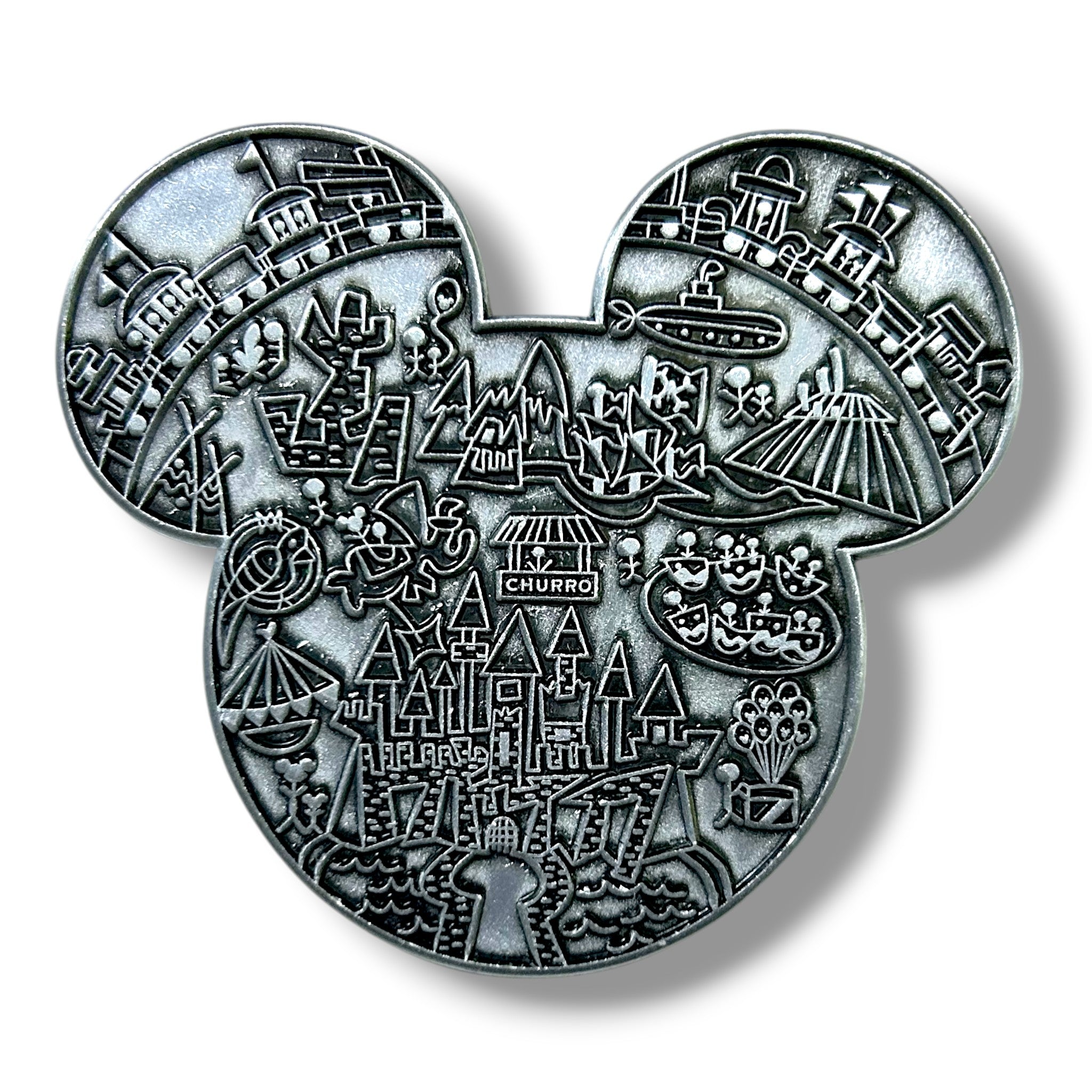 Silver enamel pin shaped like a mouse head silhouette, intricately engraved with detailed icons including a castle, mountain, rocket, pirate ship, haunted house, jungle cruise boat, teacup ride, and fireworks, creating a whimsical map-style design