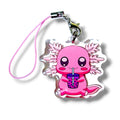 Cute cartoon-style keychain charm featuring a pink axolotl holding a cup of bubble tea. The axolotl has large round eyes, pink cheeks, and feathery gills extending from both sides of its head. It’s holding a purple bubble teacup with black tapioca pearls and a blue straw. The charm is made of clear acrylic with embedded glitter and is attached to a pink strap with a metal clasp. The design is whimsical and kawaii, perfect for fans of axolotls and boba-themed accessories.