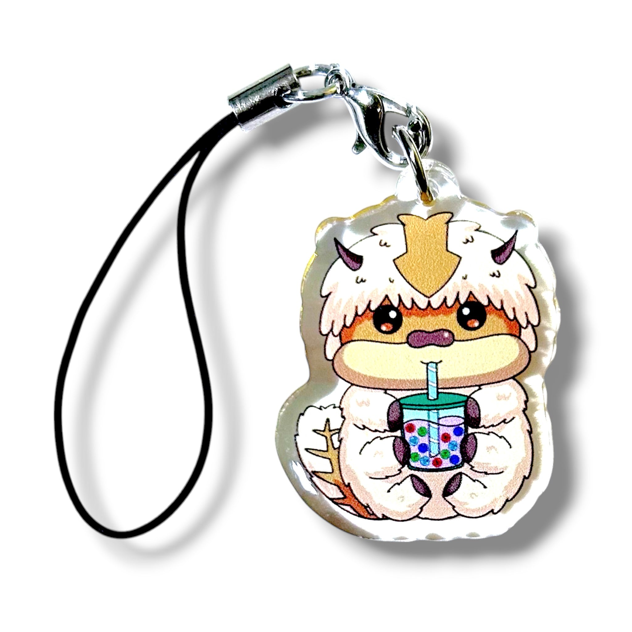 Cartoon-style keychain charm featuring a fluffy white creature with small horns, a tan face and belly, and a cheerful expression. The character is holding a bubble teacup with a blue straw and colorful tapioca pearls. The charm is made of acrylic and attached to a black strap with a silver clasp. The design combines cozy fantasy creature aesthetics with playful boba tea elements, making it a whimsical and collectible accessory.