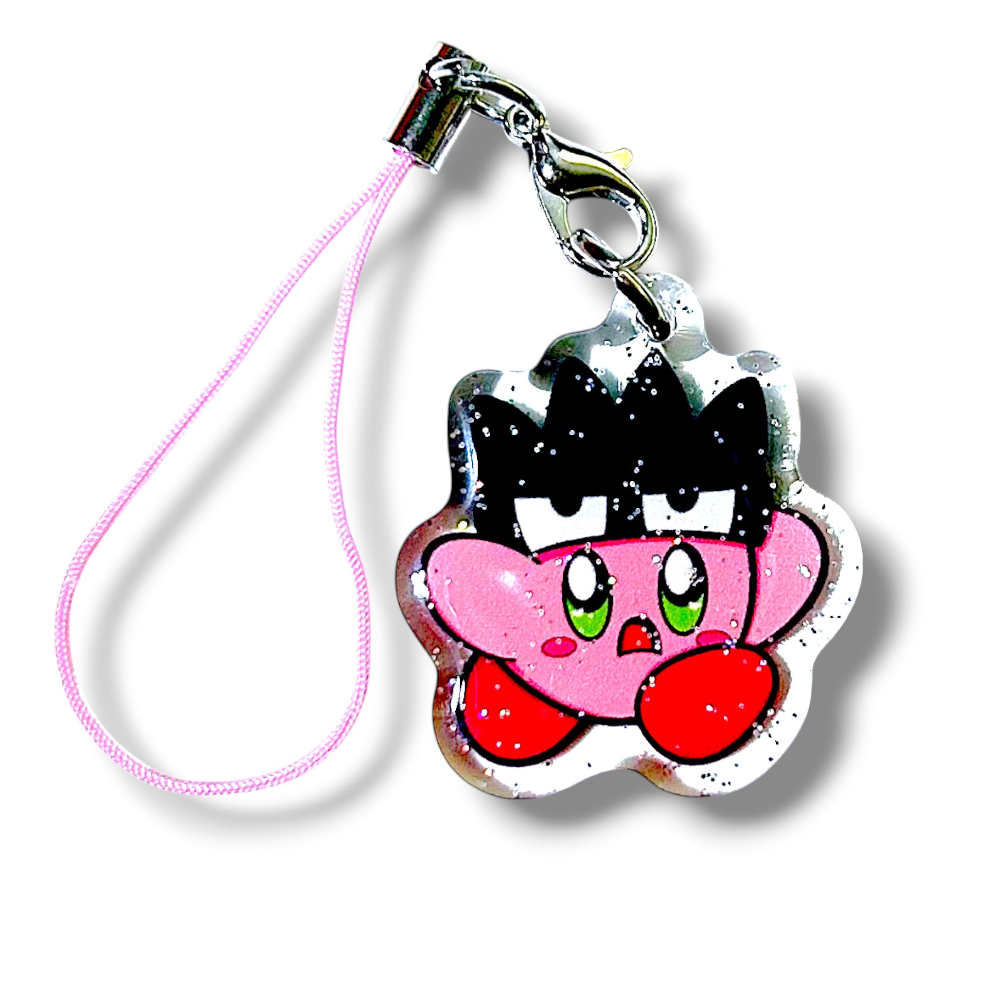 Cartoon-style keychain charm featuring a mashup character inspired by Kirby. The character has Kirby’s round pink body, red feet, and large green eyes, wearing a black crown-like headpiece with white accents. The charm has a metallic outline and is attached to a pink strap with a silver clasp and hook. The design blends cute and edgy aesthetics, making it a bold and collectible accessory for fans of video game-inspired merch.