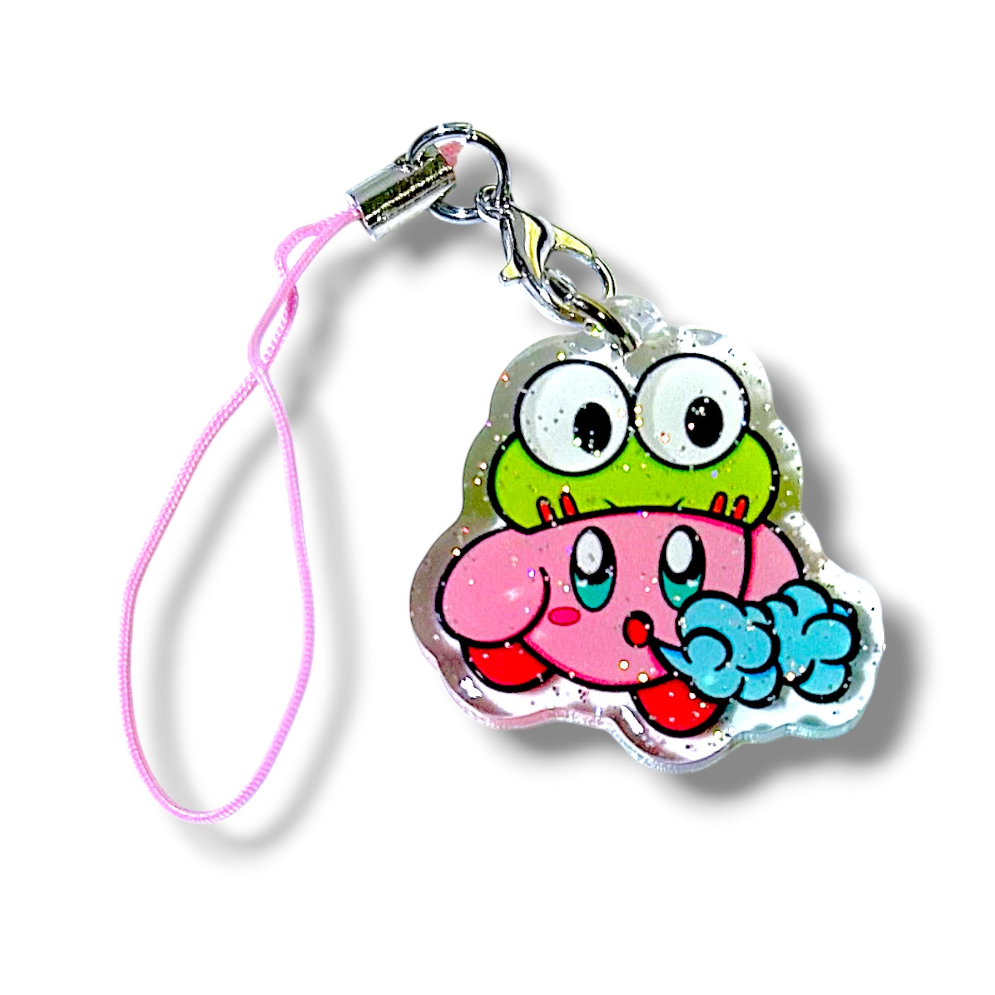 Kawaii-style keychain charm featuring Kirby wearing a frog hat and blowing a puff of air. The character has a round pink body with red feet, topped by a green frog hat with bulging eyes. The charm is made of clear acrylic with embedded glitter, giving it a sparkly finish. It’s attached to a pink strap with a metal clasp and keyring. The design blends whimsical frog flair with gamer nostalgia, making it a playful and collectible accessory.