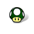 Enamel pin featuring a green mushroom with a beige stem, white spots on the cap, and two black oval eyes; designed in a cartoon style inspired by classic gaming power-ups, with a glossy finish and bold outline.