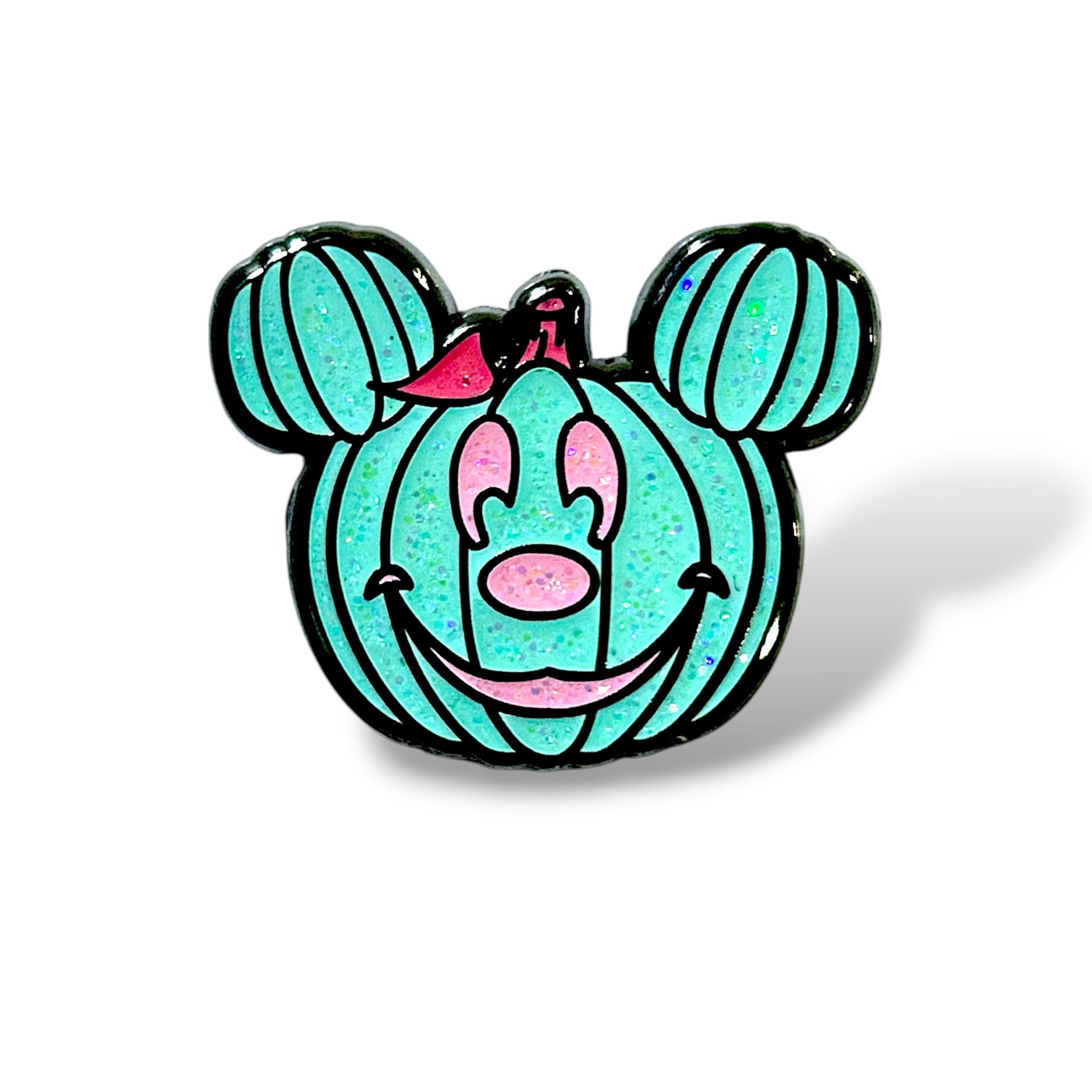 Enamel pin featuring a stylized turquoise pumpkin shaped like a cartoon mouse head, with glittery texture and black outlines. The design includes two smaller pumpkin segments as ears, pink eyes, nose, and smiling mouth, plus a pink leaf or bow on top—blending Halloween festivity with playful character-inspired charm.