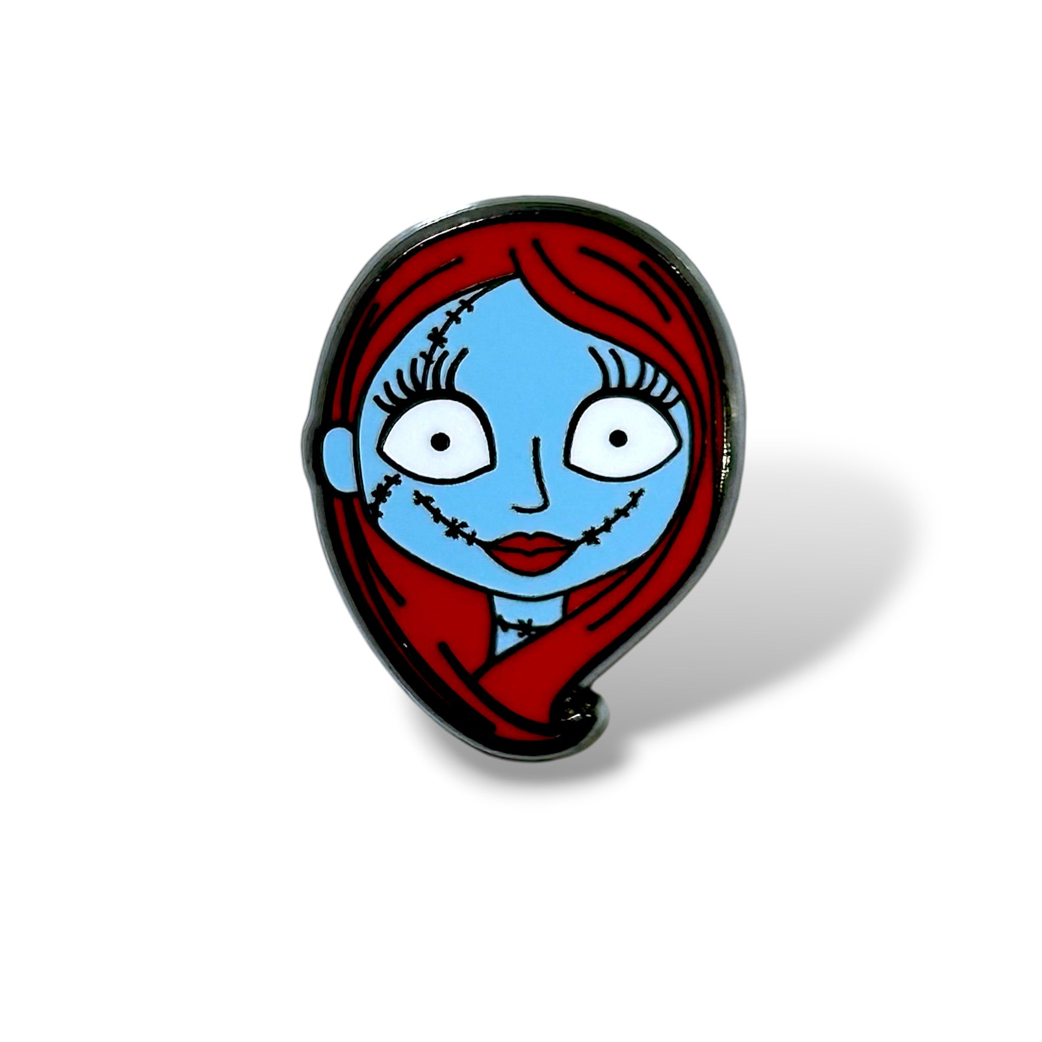 Enamel pin featuring a cartoon-style character with blue skin, large white eyes with black pupils, long black eyelashes, red lips, and flowing red hair; the face includes black stitch marks, evoking a doll-like or patchwork appearance, inspired by Halloween and spooky character themes.
