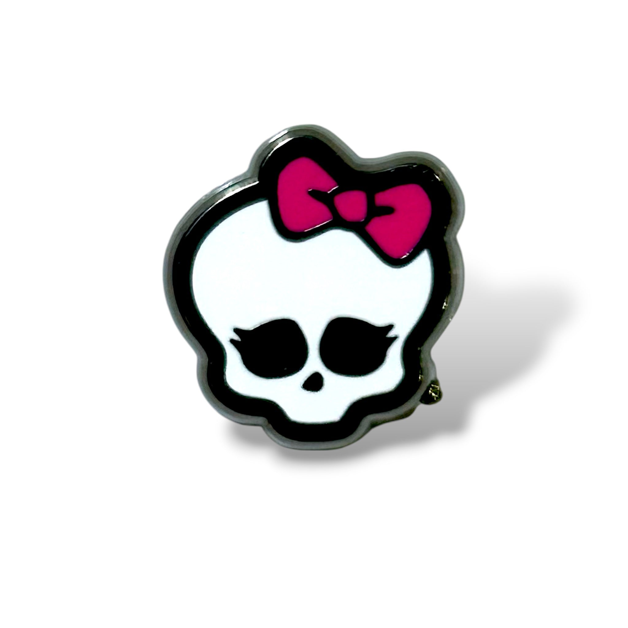 Enamel pin featuring a stylized white skull with large black eye sockets, long black eyelashes, and a small black nose cavity; topped with a bright pink bow tilted to the right. The design is outlined in black and combines spooky and playful elements, resembling a cartoon logo for a teen ghoul-themed school or brand.